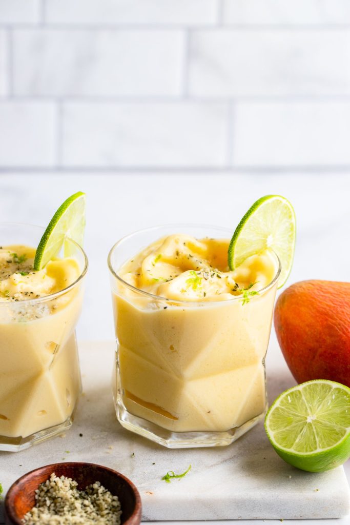 mango pineapple smoothie in glass garnished with sliced lime and lime zest.