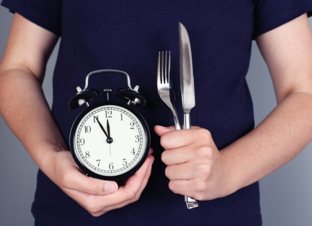 Hands holding alarm clock with fork and knife.